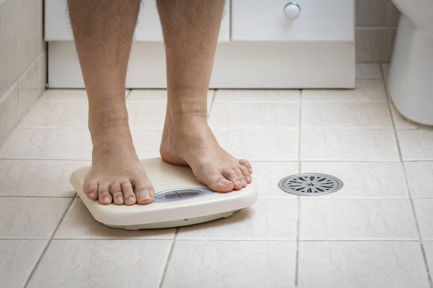 Przycięte zdjęcie stóp człowieka stojącego na skali ważenia, na podłodze w łazience - Zdjęcie, obraz