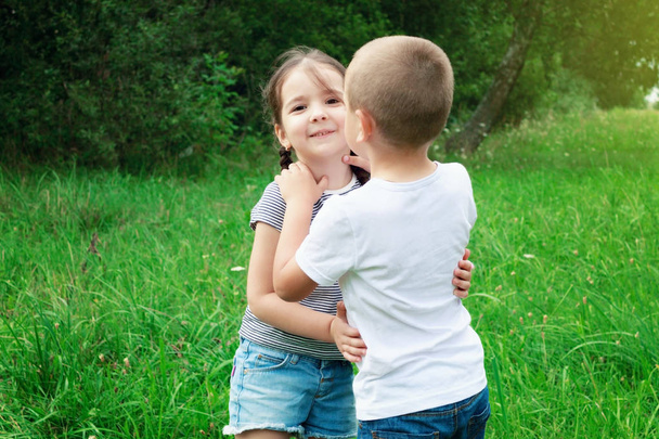 Παίζουν παιδιά - ένα αγόρι και ένα κορίτσι στη φύση. Το αγόρι αγκαλιάζει το κορίτσι. Τα παιδιά διασκεδάζουν και γέλιο - Φωτογραφία, εικόνα