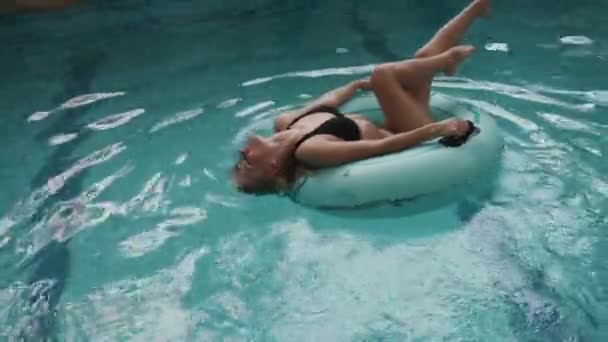 Mooie blonde vrouw met perfecte figuur in zwarte zwemmen pak is op de opblaasbare rubberring in het zwembad zwemmen. 4k. - Video