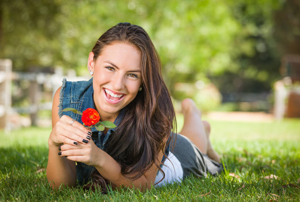 Atractivo retrato de chica de raza mixta yaciendo en hierba al aire libre con flor
. - Foto, Imagen