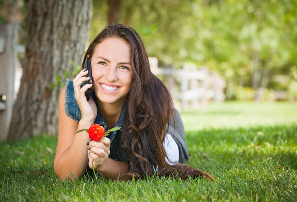 Atractivo feliz mixta raza joven hembra hablando en el teléfono celular fuera de acostarse en la hierba
. - Foto, imagen