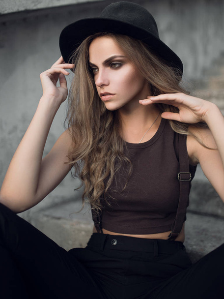 Portrait of a cute young white Caucasian girl in a black stylish hat and a short brown top. Fashion portrait of a sexy girl at sunset. - Fotoğraf, Görsel