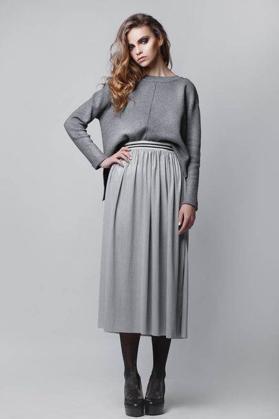 Studio portrait of a full-length stylish young girl in a gray skirt and a gray sweater on a gray background - 写真・画像