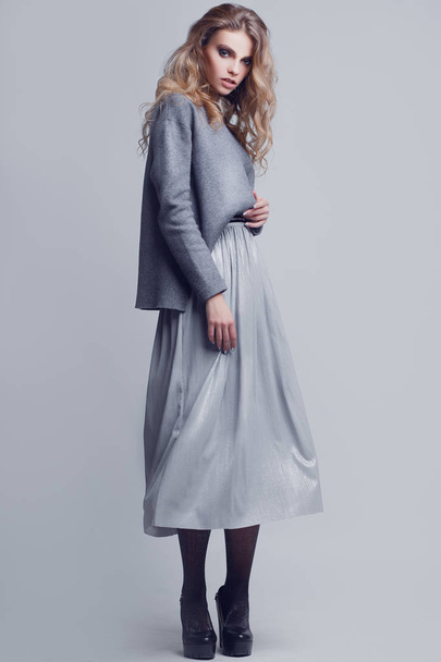 Studio portrait of a full-length stylish young girl in a gray skirt and a gray sweater on a gray background - Foto, Imagem