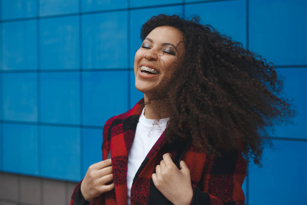 Молодая белая девушка в черном пиджаке веселится, наслаждается жизнью и улыбается на улице Минска. Ветер повалил Хайра на голову смеющейся девочки
. - Фото, изображение
