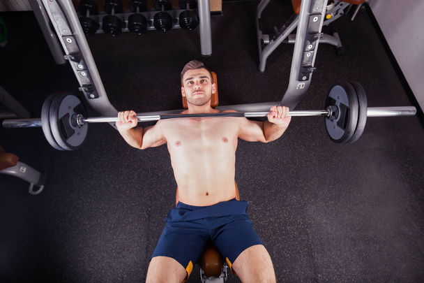Brutal athletic man pumping up muscles on bench press - Photo, image
