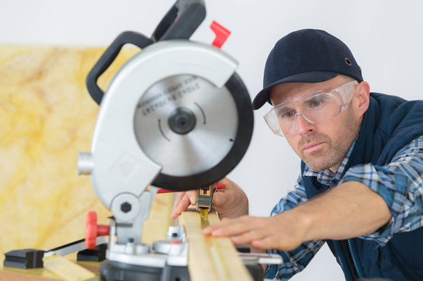 Workman using tape measure under circular saw - Fotó, kép