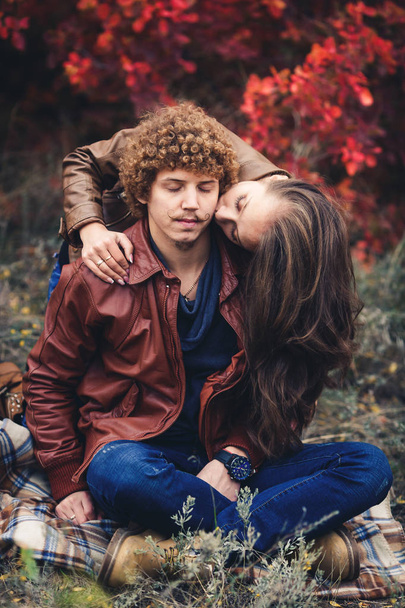 Curly-haired mustachioed man and brown-haired woman hugging in autumn against background of red trees. - Fotoğraf, Görsel