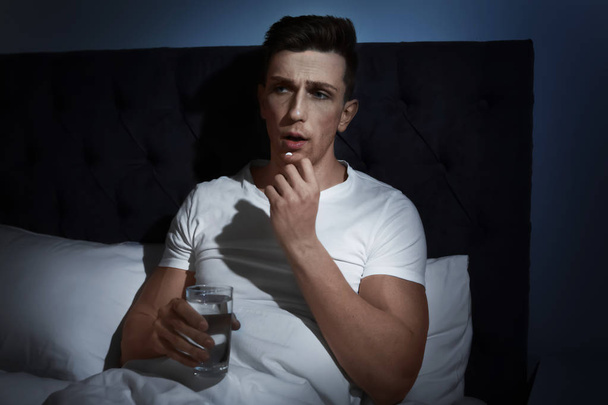 Junger Mann mit schrecklichen Kopfschmerzen nimmt nachts Tabletten im Bett - Foto, Bild