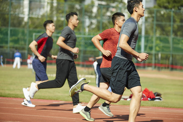 jonge Aziatische volwassen atleten opleiding lopen op schema, zijaanzicht. - Foto, afbeelding