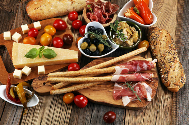 Italian antipasti wine snacks set. Cheese variety, Mediterranean olives, crudo, Prosciutto di Parma, salami and wine in glasses over wooden grunge background - Photo, Image