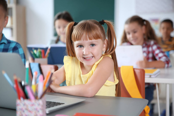 Słodkie małe dziecko z laptopa siedząc przy biurku w klasie. Szkoła podstawowa - Zdjęcie, obraz