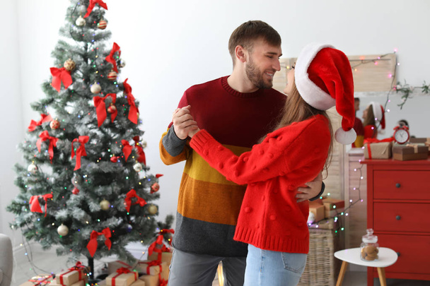 Happy young couple dancing near Christmas tree at home - Foto, imagen