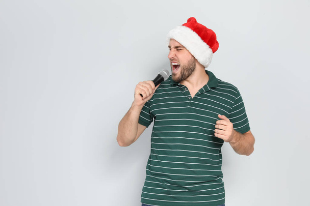 Young man in Santa hat singing into microphone on color background. Christmas music - Фото, зображення