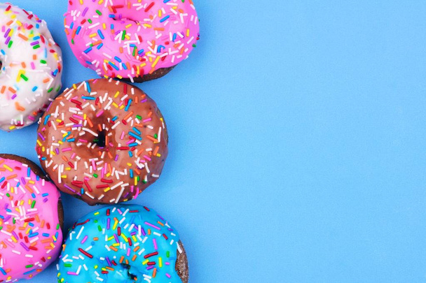 Seitenrand aus verschiedenen Donuts mit Zuckerguss und Streusel vor pastellblauem Hintergrund - Foto, Bild