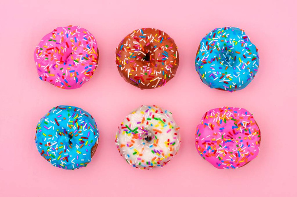 Six assorted donuts with pastel colored icing and sprinkles against a soft pink background. Minimal concept. - Fotografie, Obrázek