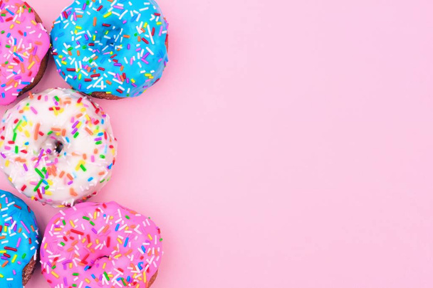 Seitenrand aus verschiedenen Donuts mit Zuckerguss und Streusel vor pastellrosa Hintergrund - Foto, Bild