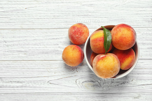 Bowl with delicious ripe peaches on wooden background, top view - Foto, imagen