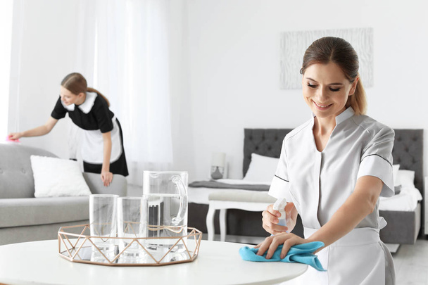 Professional chambermaid cleaning table in hotel room - Φωτογραφία, εικόνα