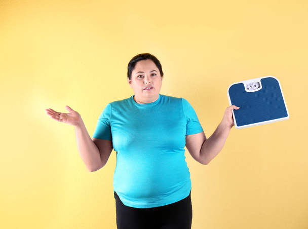 Overweight woman in sportswear with scales on color background - Photo, image