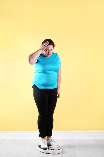 Overweight woman in sportswear using scales near color wall - Φωτογραφία, εικόνα