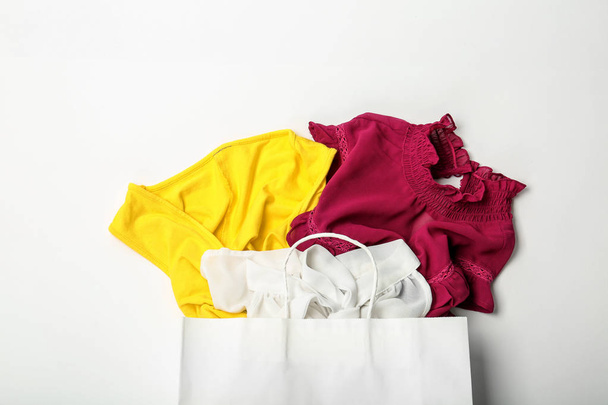 Κομψή επίπεδη σύνθεση με τσάντα για ψώνια και ρούχα Βάλτε σε λευκό φόντο - Φωτογραφία, εικόνα