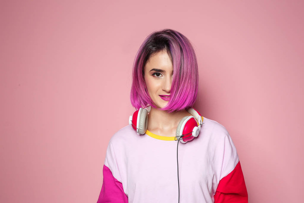 Young woman with trendy hairstyle and headphones against color background - Foto, Imagen