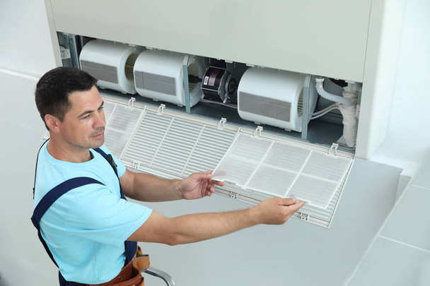 Male technician cleaning air conditioner indoors - Foto, imagen