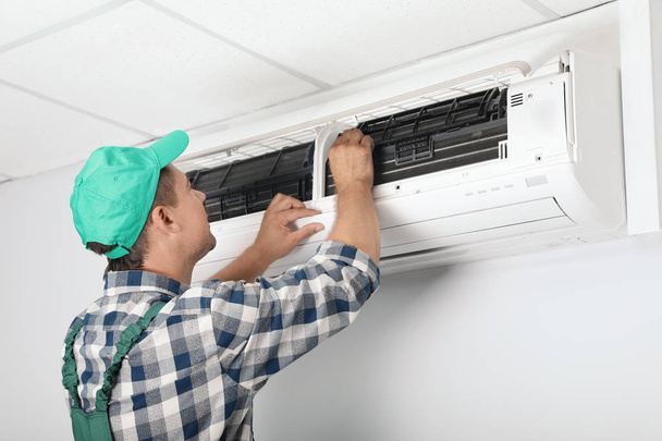 Male technician cleaning air conditioner indoors - Φωτογραφία, εικόνα