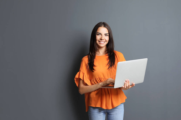 Young woman with modern laptop on grey background - Zdjęcie, obraz