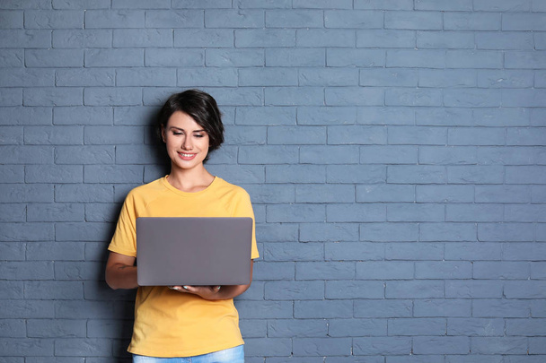 Young woman with modern laptop on brick wall background - Fotoğraf, Görsel