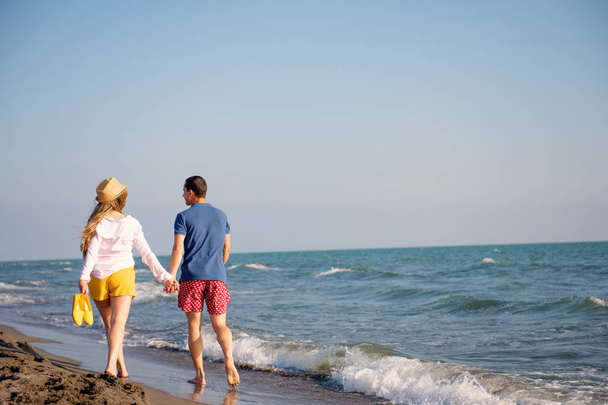 ξέγνοιαστες άνδρας και η γυναίκα το περπάτημα στη θάλασσα ακτή, ΠΙΣΩ ΟΨΗ - Φωτογραφία, εικόνα