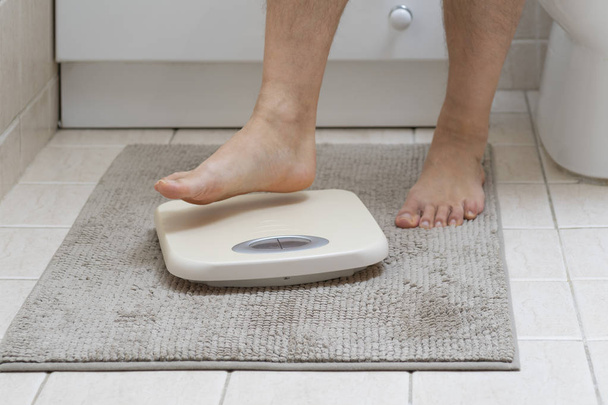Bijgesneden afbeelding van man voeten intensivering op weegschalen, op de badkamervloer - Foto, afbeelding