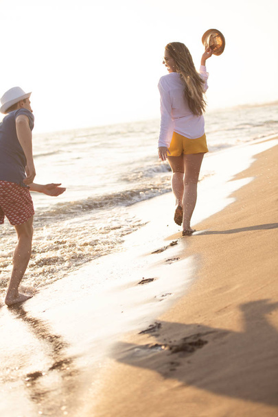 ξέγνοιαστες άνδρας και η γυναίκα το περπάτημα στη θάλασσα ακτή, ΠΙΣΩ ΟΨΗ - Φωτογραφία, εικόνα