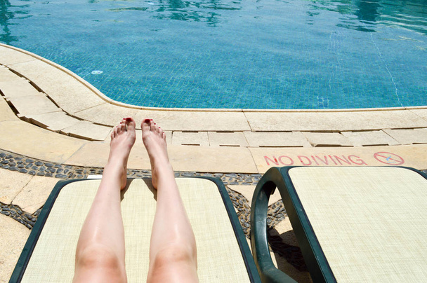 美脚、女の子の足、暖かい熱帯のエキゾチックなシーサイド リゾートのプールとデッキチェアの背景に赤のマニキュアの女性夏の休暇 - 写真・画像