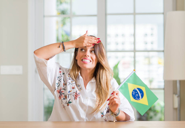 若い女性自宅で強調したブラジルの旗を保持して頭、恥とショックに手し、驚き顔、怒っているとイライラ。恐怖と動揺の間違い. - 写真・画像