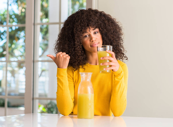 African american woman drinking healthy fruit juice at home pointing with hand and finger up with happy face smiling - Photo, image