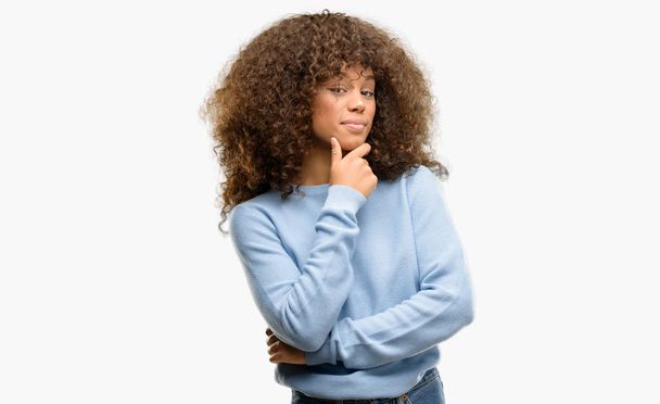 Femme afro-américaine portant un pull regardant avec confiance la caméra avec le sourire avec les bras croisés et la main levée sur le menton. Penser positif
. - Photo, image