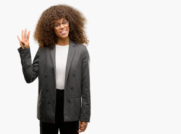 African american business vrouw dragen bril tonen en met vingers omhoog nummer vier terwijl lacht zelfverzekerd en blij. - Foto, afbeelding
