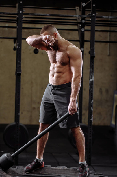 strong sportsman is resting after workingout with hammer - Photo, Image