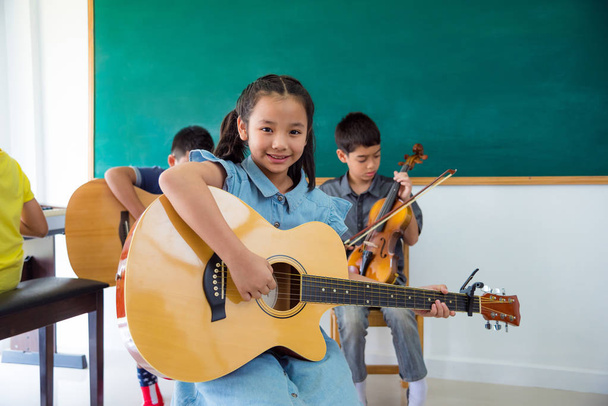 Pretty asian girl smiling with guitar in school classroom - Photo, Image