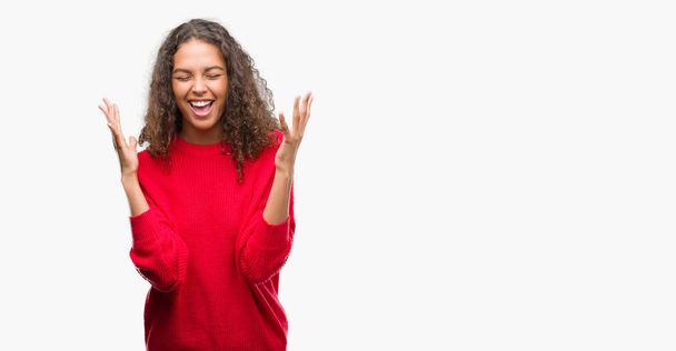 Mujer hispana joven vistiendo suéter rojo celebrando loco y loco por el éxito con los brazos levantados y los ojos cerrados gritando emocionados. Concepto ganador
 - Foto, Imagen