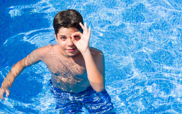 Bambino in vacanza in piscina vicino alla spiaggia con il viso felice sorridente facendo ok segno con mano sugli occhi guardando attraverso le dita
 - Foto, immagini