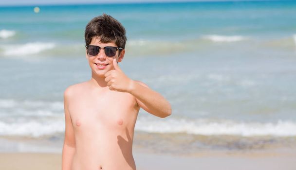 Criança em férias na praia feliz com grande sorriso fazendo sinal ok, polegar com os dedos, excelente sinal
 - Foto, Imagem