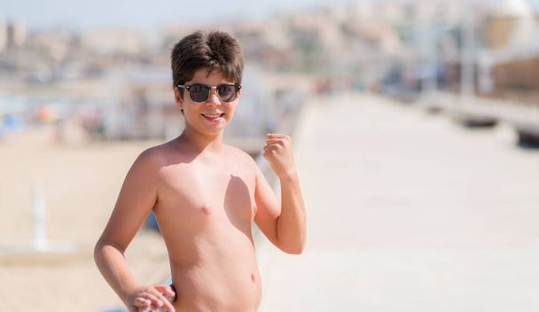 Niño pequeño en vacaciones en la playa gritando orgulloso y celebrando la victoria y el éxito muy emocionado, animando emoción
 - Foto, imagen