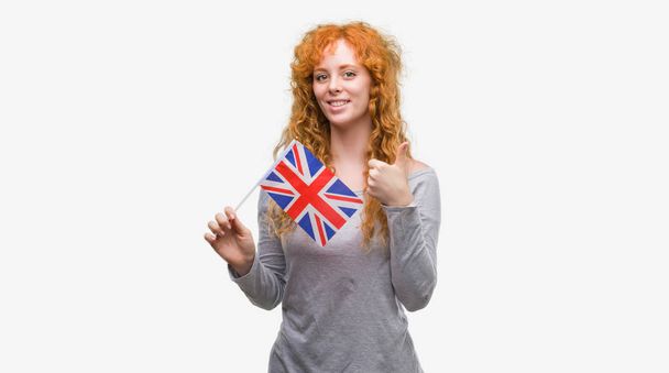 笑顔の ok サイン、指、優秀な兆候を親指をやって幸せなイギリスの旗を保持している赤毛の若い女性 - 写真・画像