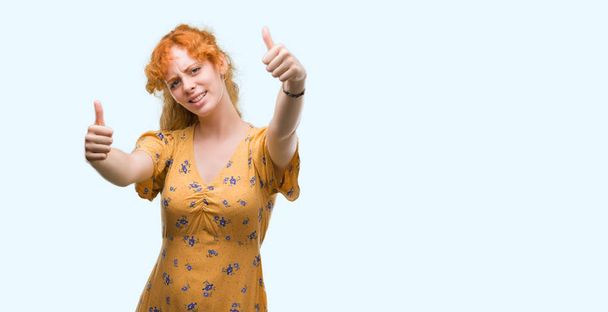 承認若い赤毛の女性は、笑顔と幸せな成功のため親指の手で肯定的なジェスチャーをしています。カメラ、勝者のジェスチャーを見てください。. - 写真・画像