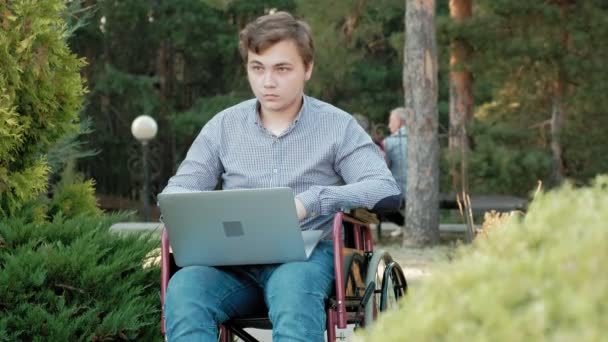 Engelli biri tekerlekli sandalyede oturan ve parkta bir dizüstü bilgisayar üzerinde çalışan - Video, Çekim