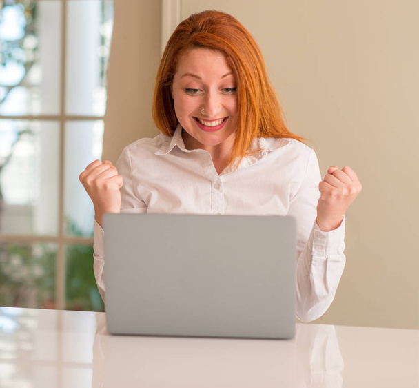 Mulher ruiva usando laptop computador em casa gritando orgulhoso e celebrando vitória e sucesso muito animado, torcendo emoção
 - Foto, Imagem