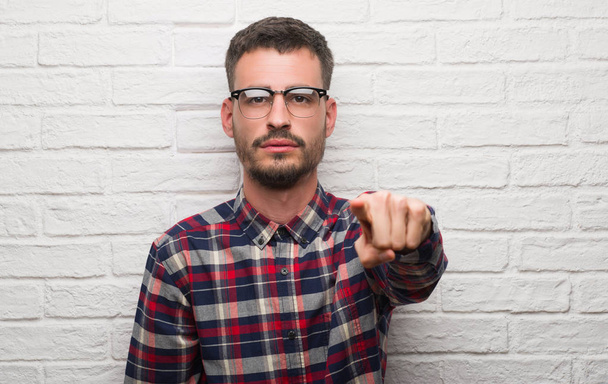 Young adult man standing over white brick wall pointing with finger to the camera and to you, hand sign, positive and confident gesture from the front - Photo, Image